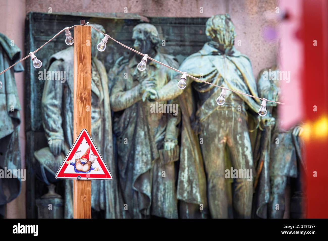 Attenzione pericolo di scivolamento cartello con Heinzelmaennchen davanti alle figure del monumento equestre per l'imperatore Federico Guglielmo III a Heumarkt Foto Stock