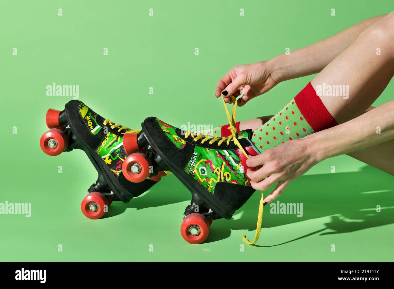 Vista laterale del ritaglio di graffette femminili anonime e posizionamento di lame a rulli retrò colorate contro la parete verde durante il pattinaggio a rotelle Foto Stock