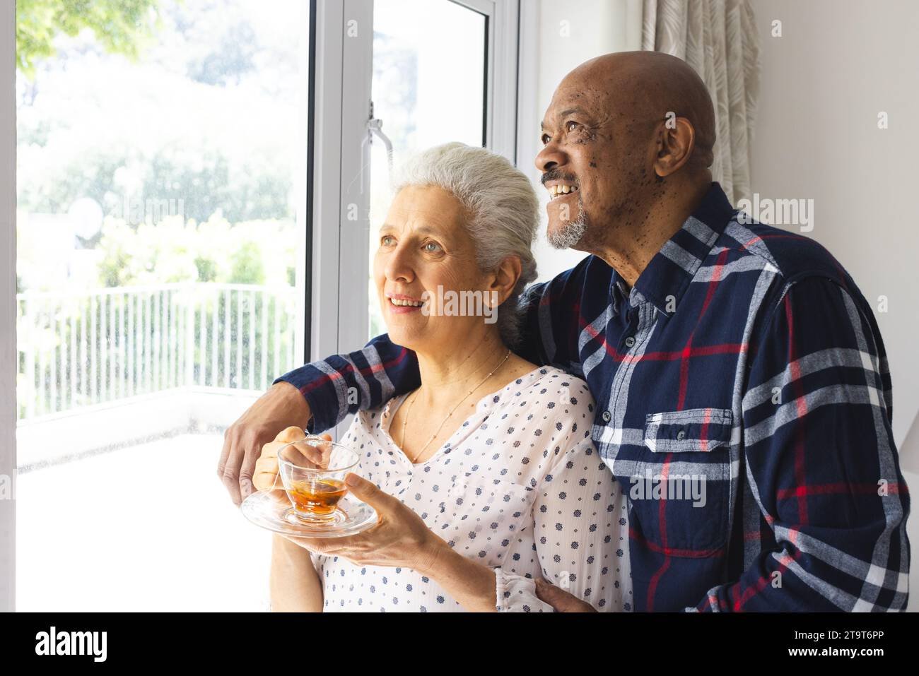 Diverse coppie anziane che bevono tè, abbracciano e guardano fuori dalla finestra della soleggiata casa. Stile di vita, pensionamento, stile di vita senior, unicità e domestico Foto Stock