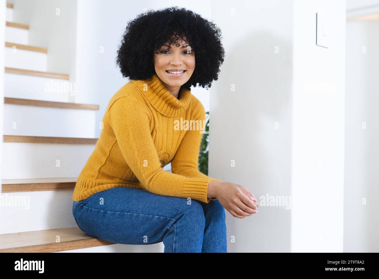 Felice donna afro-americana seduta sulle scale a casa, spazio fotocopie. All'interno, espressione, gesticolazione, linguaggio del corpo e femminilità, inalterati. Foto Stock