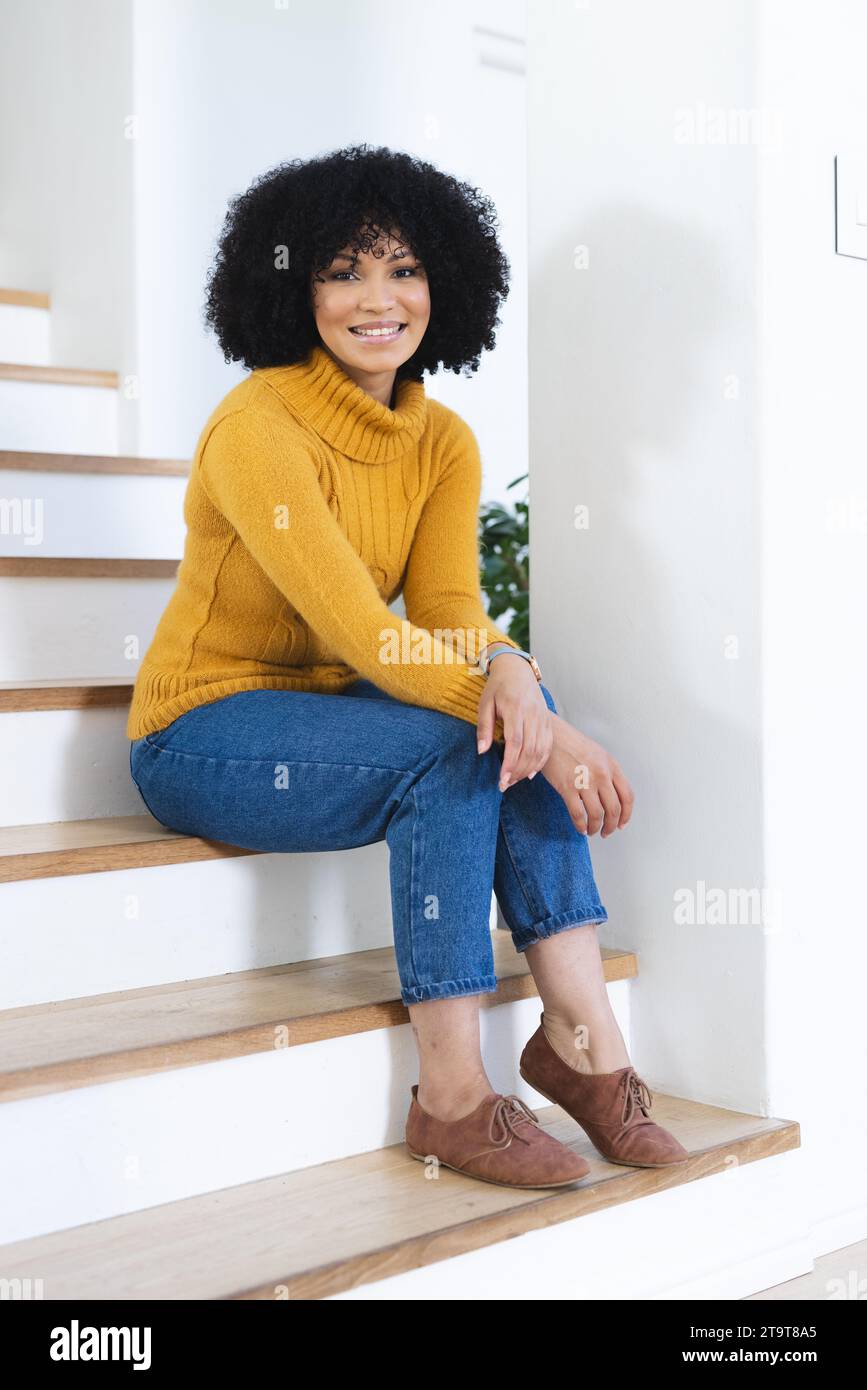Felice donna afro-americana seduta sulle scale a casa, spazio fotocopie. All'interno, espressione, gesticolazione, linguaggio del corpo e femminilità, inalterati. Foto Stock
