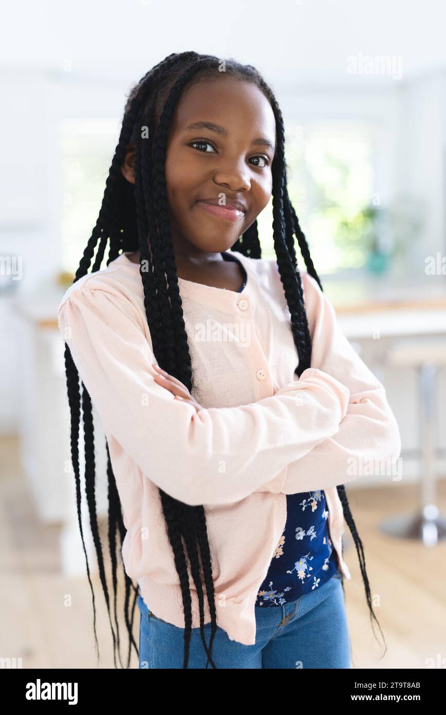 Felice ragazza afro-americana in piedi con le braccia incrociate a casa, spazio per copiare. Infanzia, espressione, gesticolazione e vita domestica, inalterati. Foto Stock