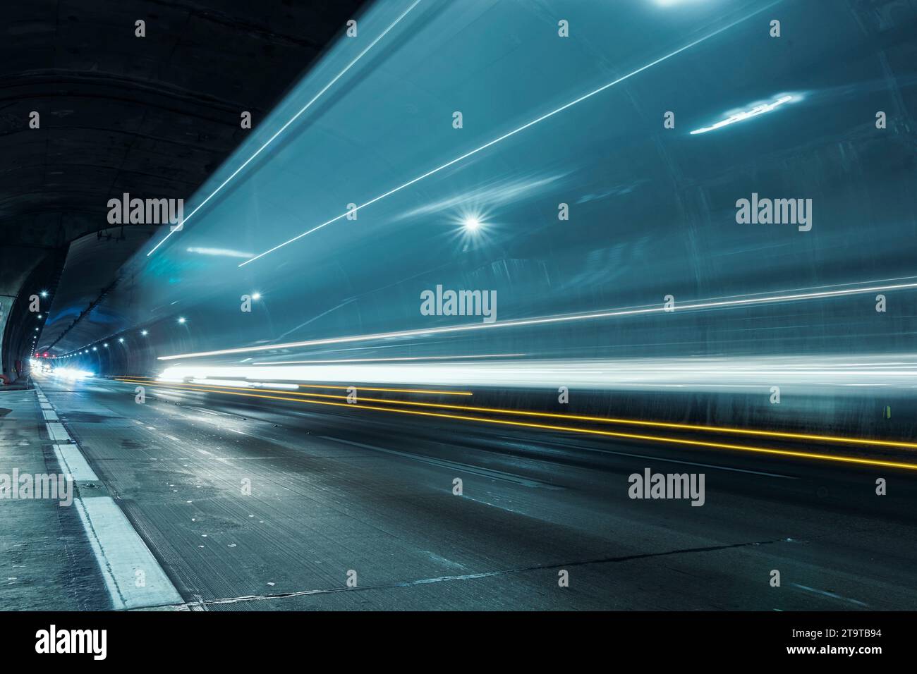 Sentieri di luci per auto che passano velocemente attraverso il tunnel dell'autostrada in prospettiva. Foto Stock