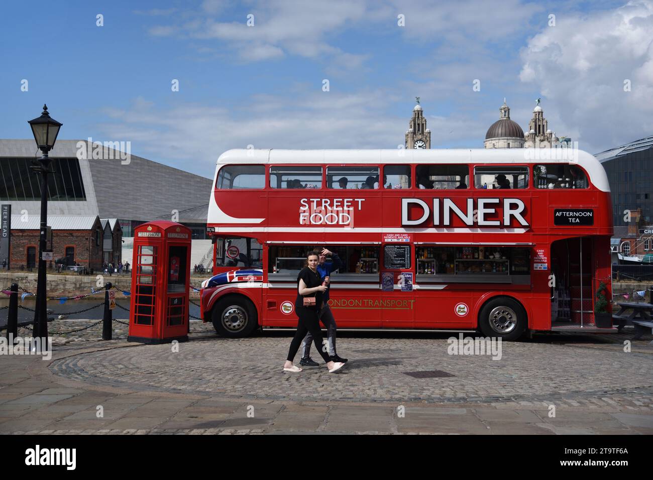 I turisti camminano accanto all'autobus rosso a due piani convertito in Street Food Diner, Food Truck o ristorante sul lungomare o Pier Head Liverpool Inghilterra Regno Unito Foto Stock