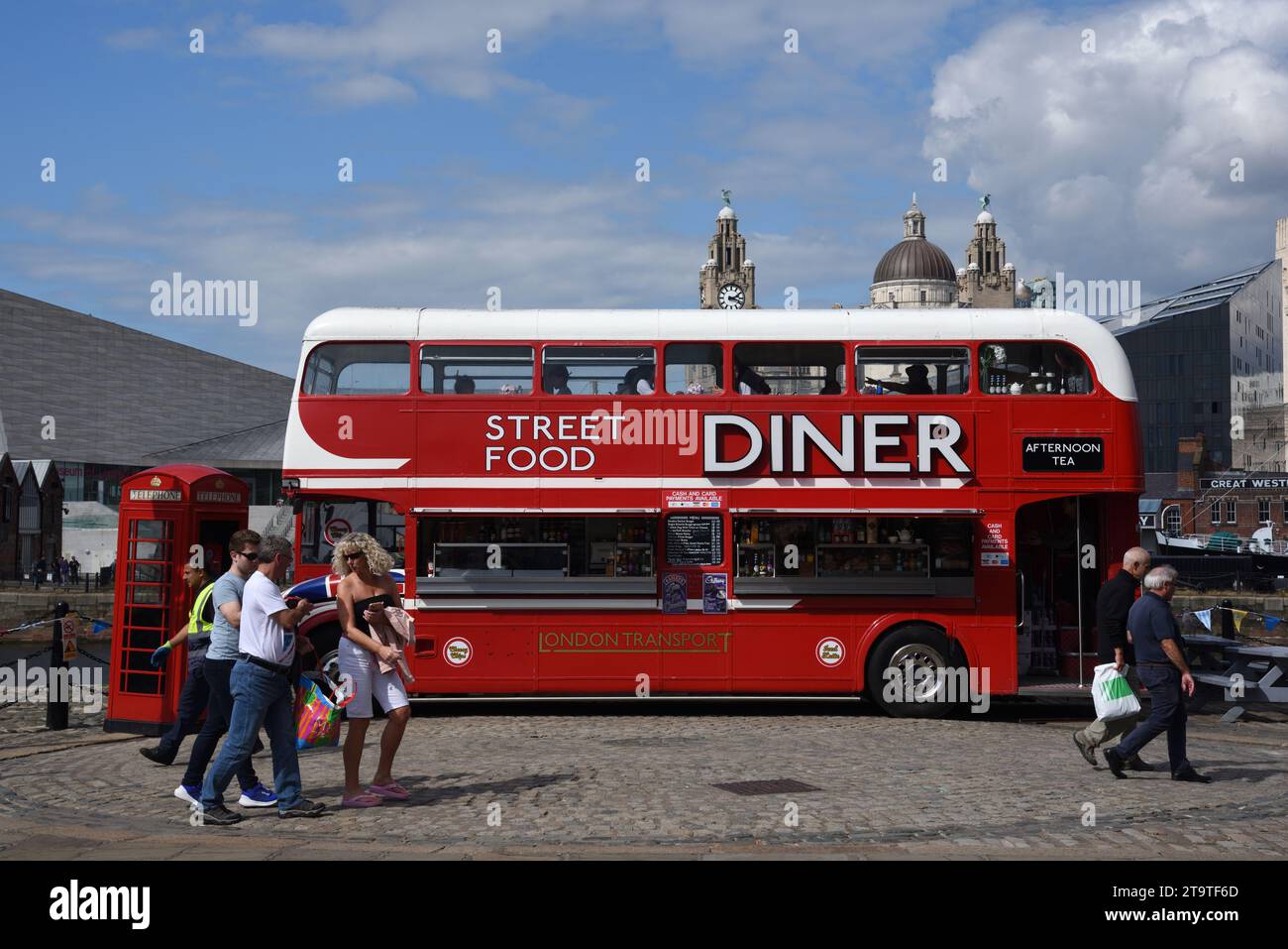 I turisti camminano accanto all'autobus rosso a due piani convertito in Street Food Diner, Food Truck o ristorante sul lungomare o Pier Head Liverpool Inghilterra Regno Unito Foto Stock