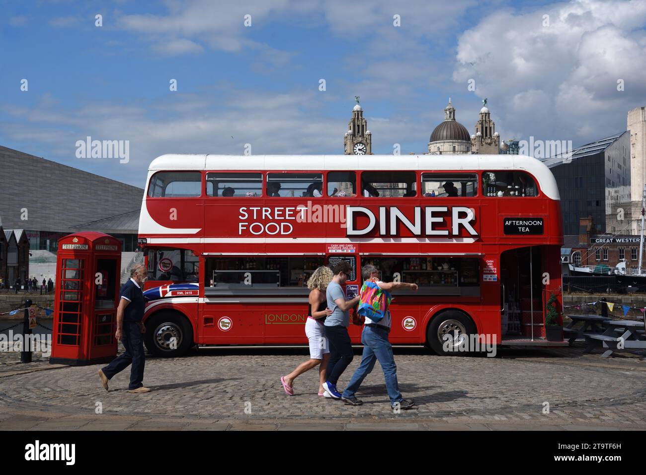 I turisti camminano accanto all'autobus rosso a due piani convertito in Street Food Diner, Food Truck o ristorante sul lungomare o Pier Head Liverpool Inghilterra Regno Unito Foto Stock