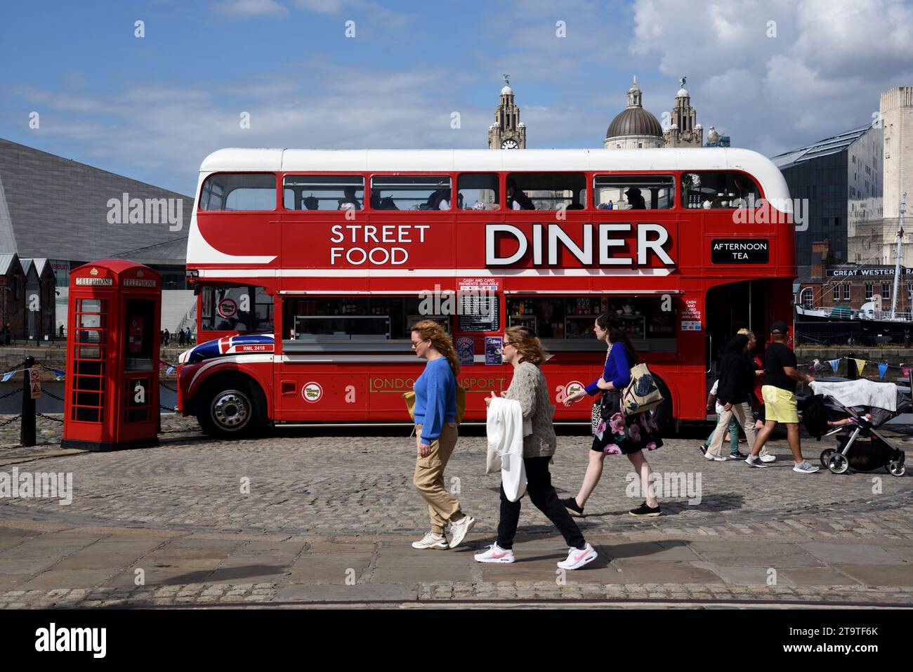 I turisti camminano accanto all'autobus rosso a due piani convertito in Street Food Diner, Food Truck o ristorante sul lungomare o Pier Head Liverpool Inghilterra Regno Unito Foto Stock