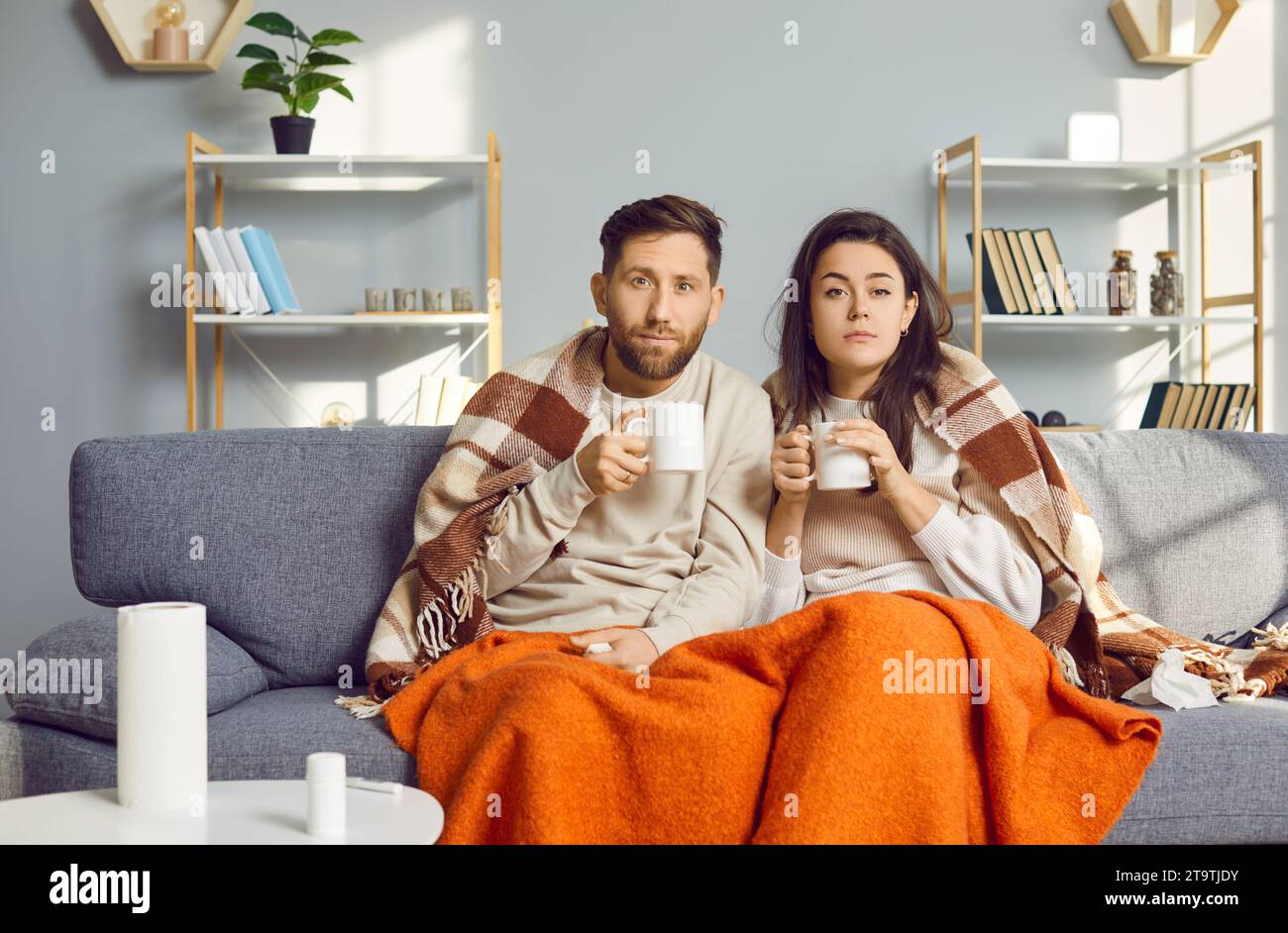 Giovane coppia malata coperta di coperte seduta sul divano a casa con influenza stagionale o freddo. Foto Stock