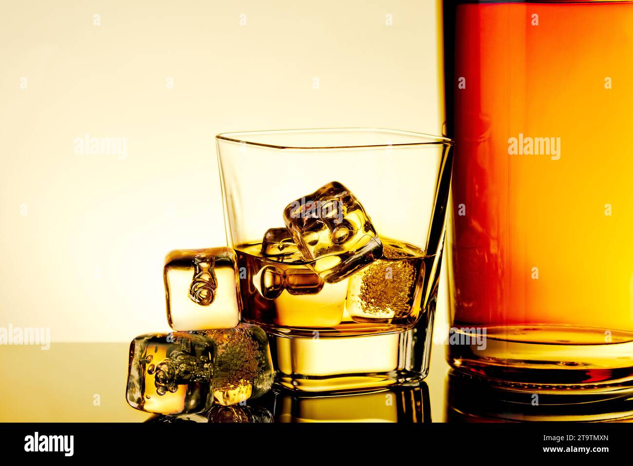 bicchiere di whisky con cubetti di ghiaccio vicino alla bottiglia e cubetti di ghiaccio sul tavolo con riflesso, calda atmosfera di tinta, tempo di relax con whisky Foto Stock