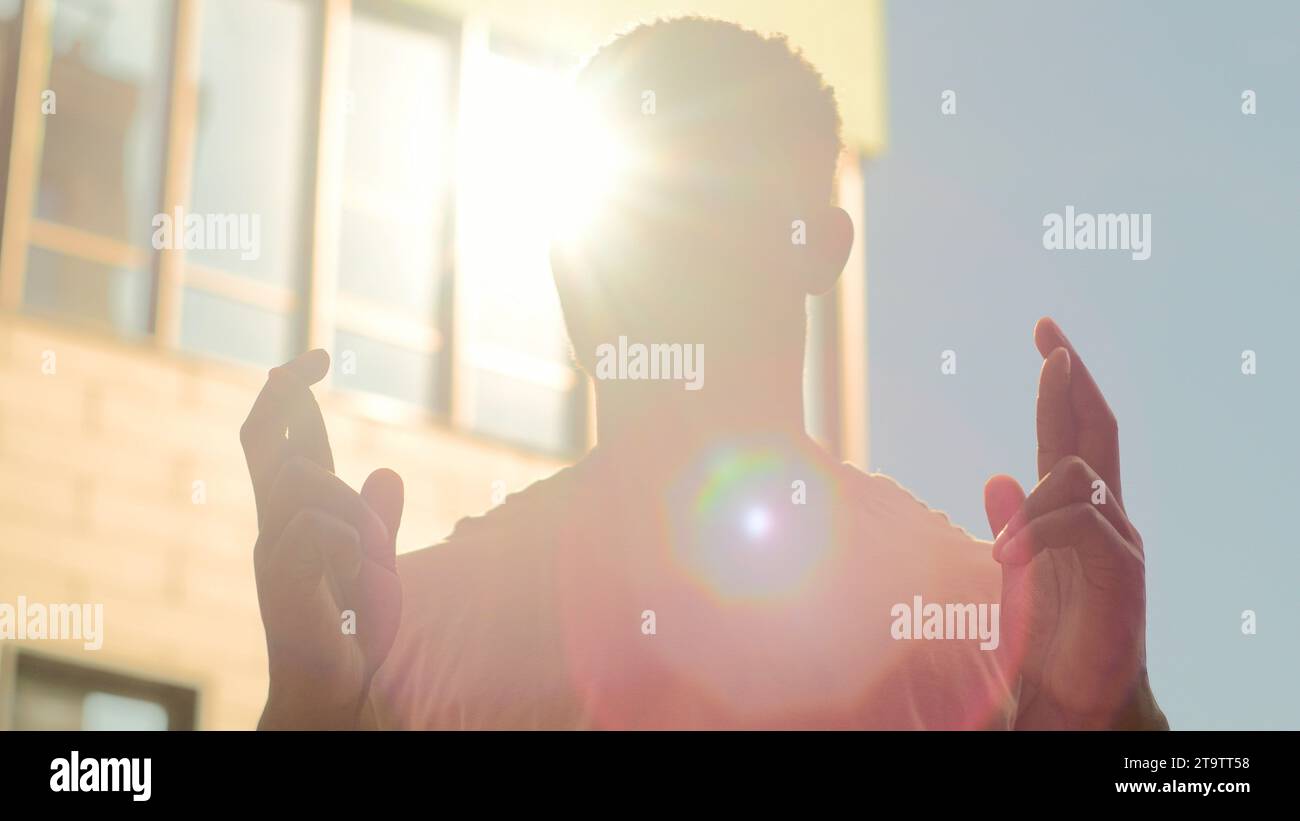 Uomo afroamericano silhouette maschile in sole sole sole sfondo sunbeam Guy crossing Fingers Wish Pray Chiedi a dio fortuna fortuna pregando desiderio Foto Stock