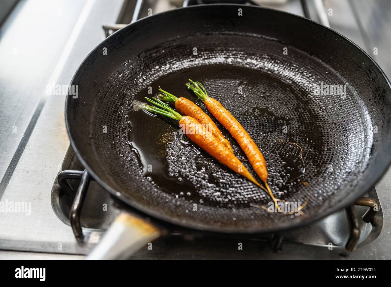 Le carote friggono in padella oliata in una stufa a gas in una cucina professionale in un ristorante. Immagine del concetto di cucina di un hotel di lusso. Foto Stock