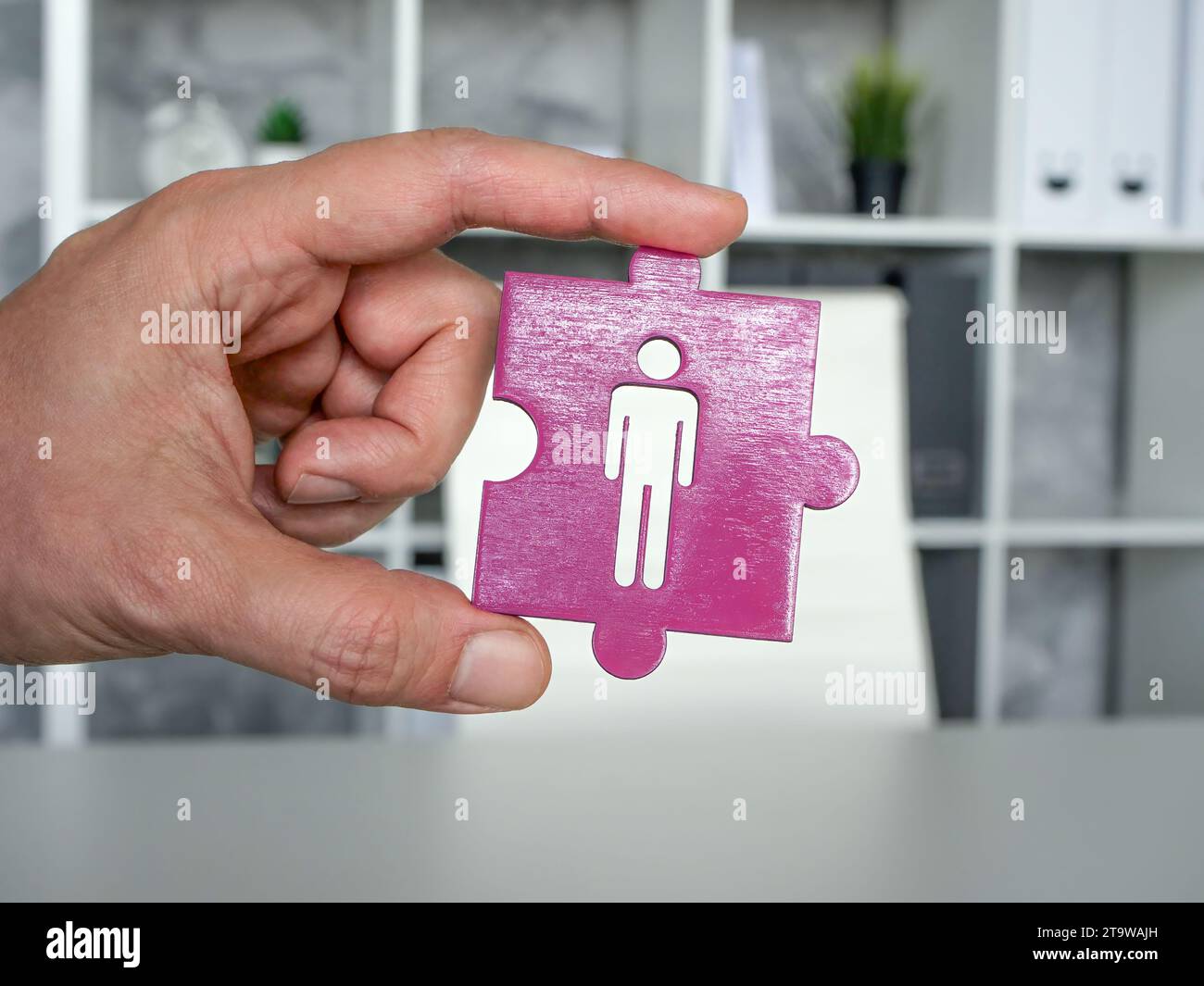 Concetto di onboarding e reclutamento. Una mano tiene il pezzo del puzzle vicino al banco di lavoro. Foto Stock