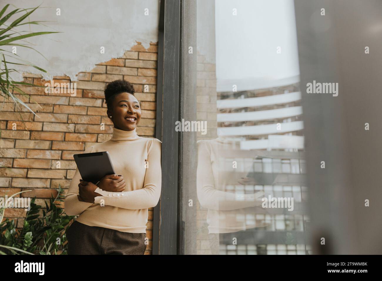 Una bella giovane donna d'affari afroamericana con un tablet digitale in piedi accanto al muro in stile industriale Foto Stock