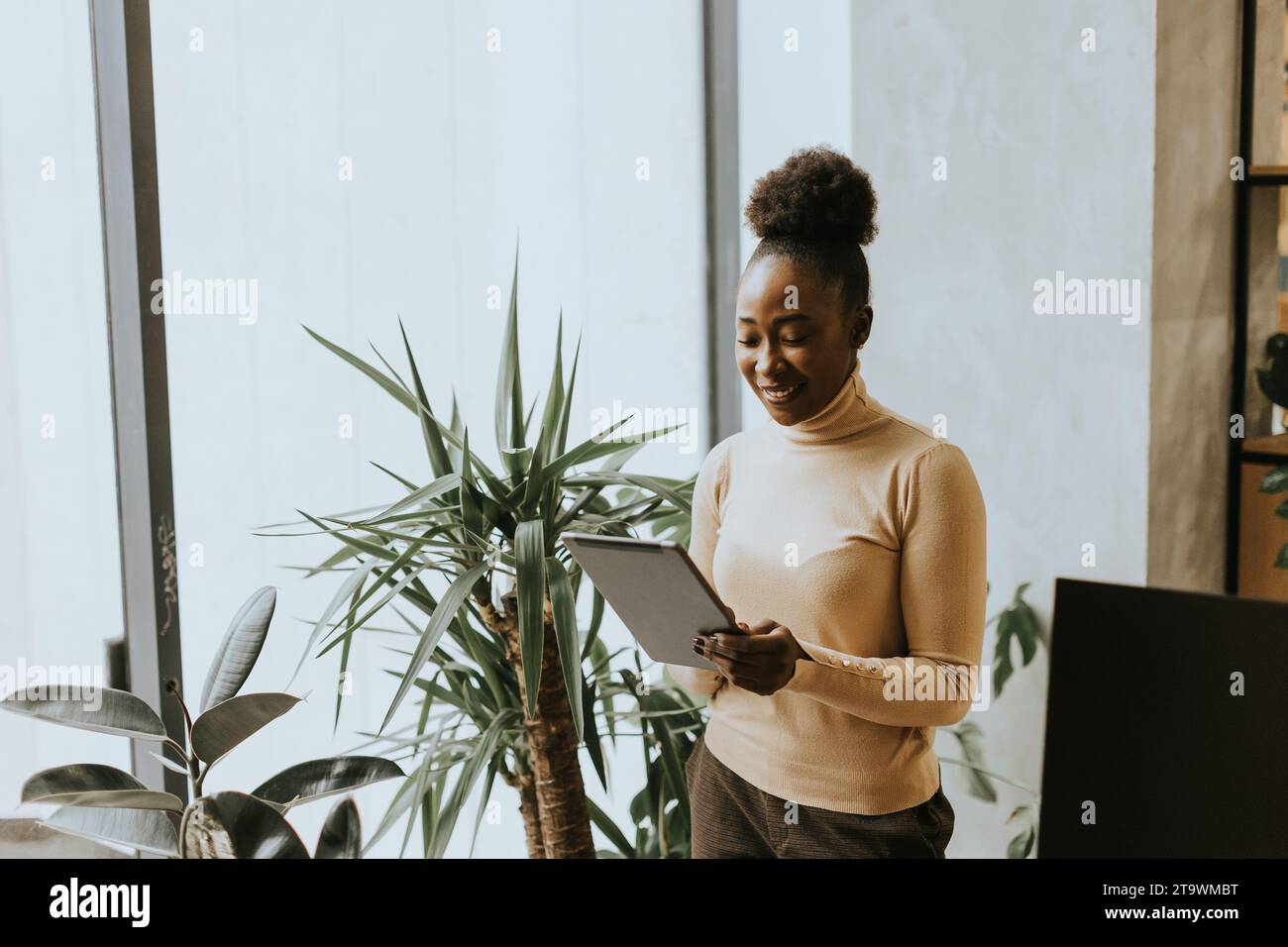 Una bella giovane donna d'affari afroamericana con un tablet digitale a parete in ufficio Foto Stock