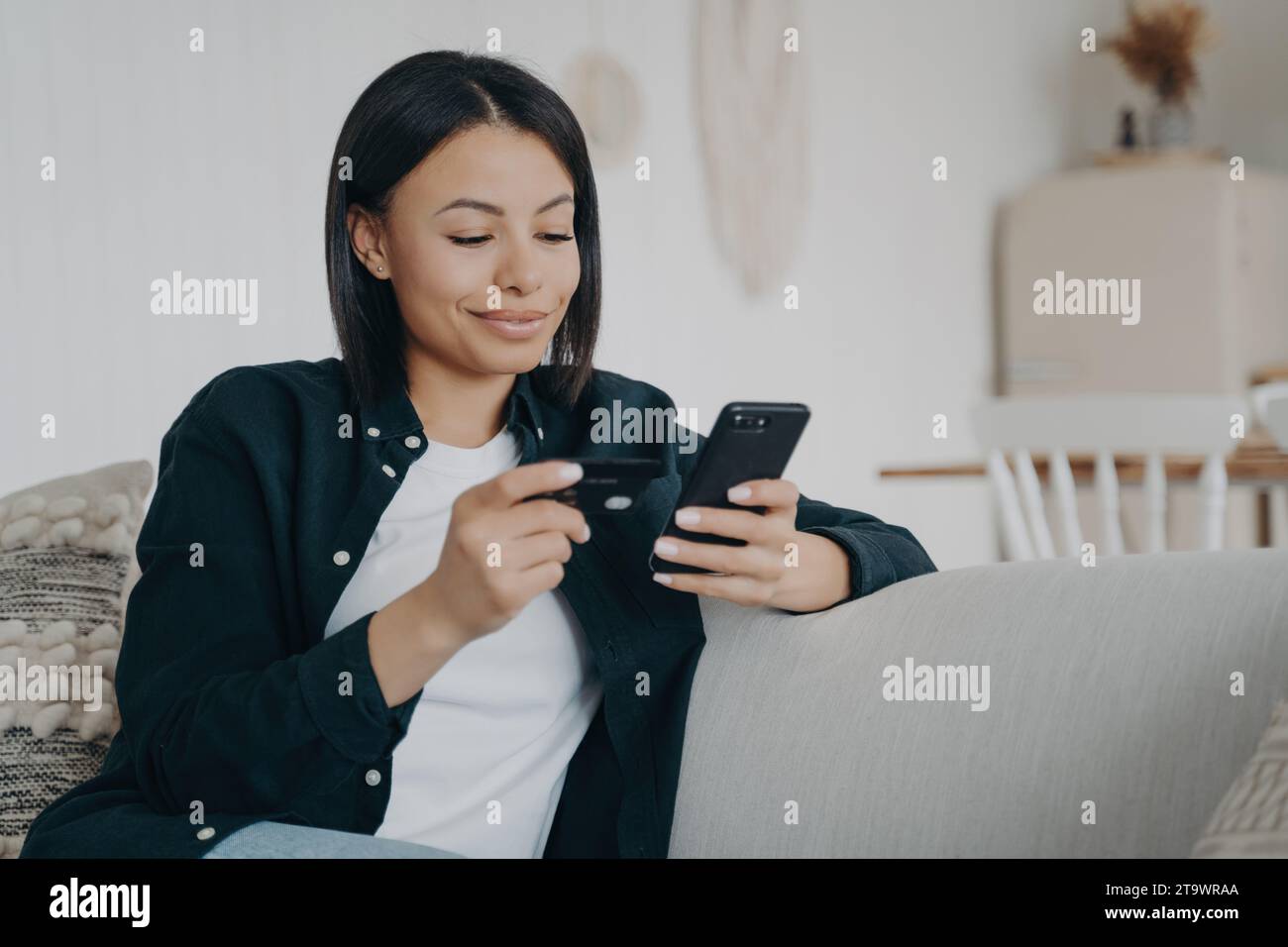 Giovane donna sorridente che usa lo smartphone per l'online banking a casa Foto Stock