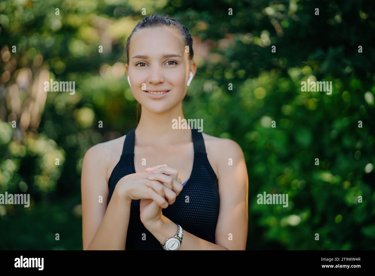 In forma, giovane donna con le cuffie, sorridendo in un parco lussureggiante, dopo l'allenamento Foto Stock