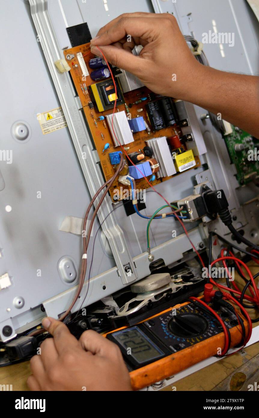 Cairo, Egitto, 3 ottobre 2023: Ingegnere tecnico che utilizza un multimetro digitale, circuito di alimentazione della scheda principale TV LCD, fili, trasformatori, resis Foto Stock