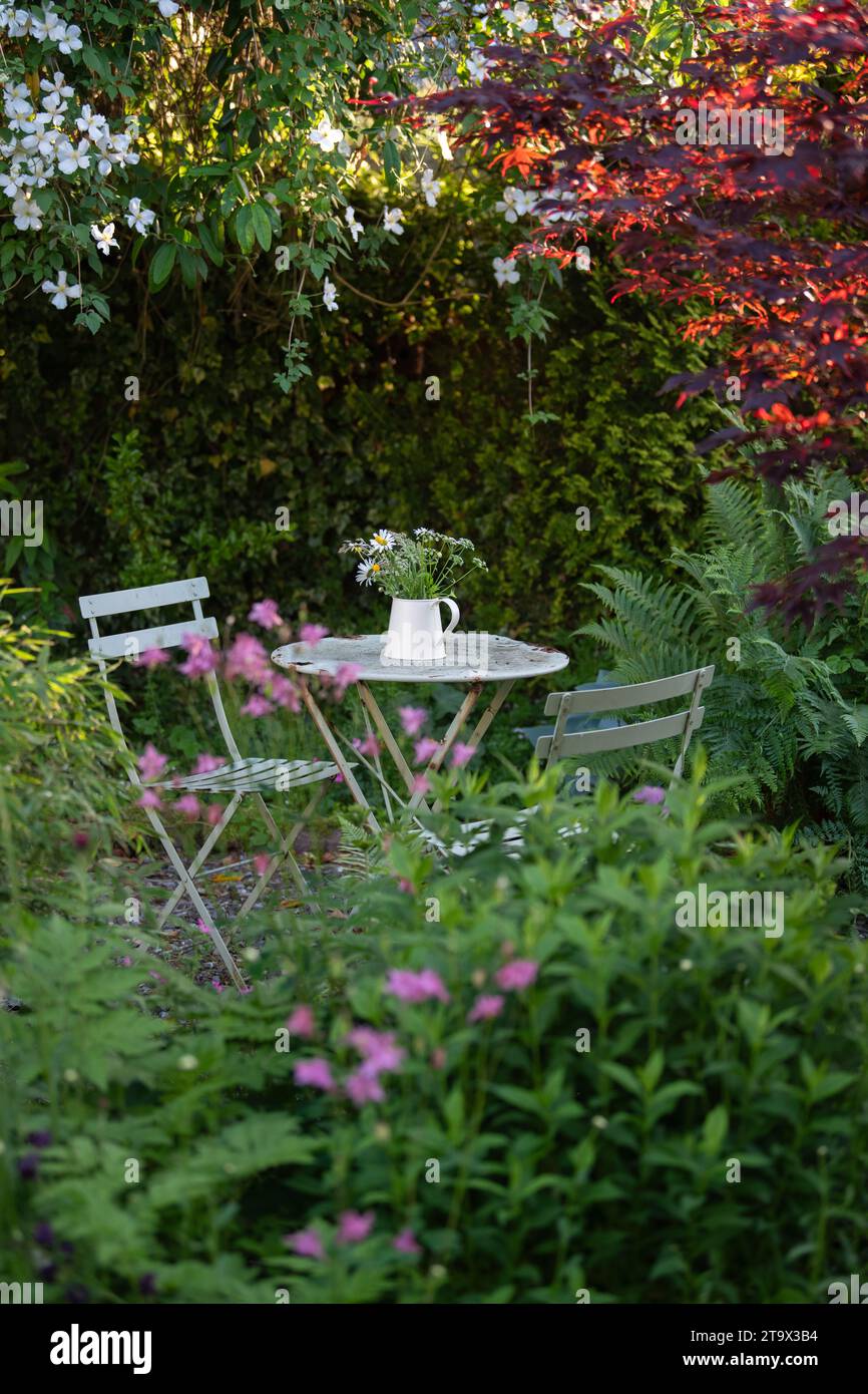 Area salotto in giardino appartata all'ombra con tavolo e sedie in stile caffe' di metallo e caraffa di fiori - UK Foto Stock