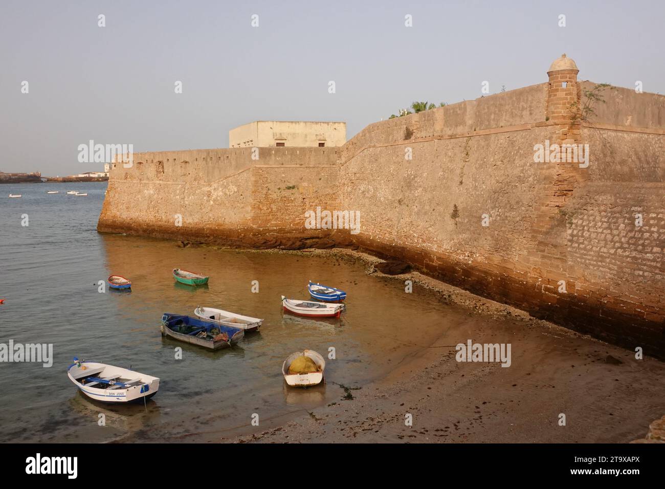 Barche da pesca ormeggiate dalle mura del Castillo de Santa Catalina lungo la spiaggia di Cadice, in Spagna. Il castello a forma di pentagono fu costruito dopo che gli inglesi saccheggiarono la città nel 1596 per proteggere la baia di Cadice. Foto Stock