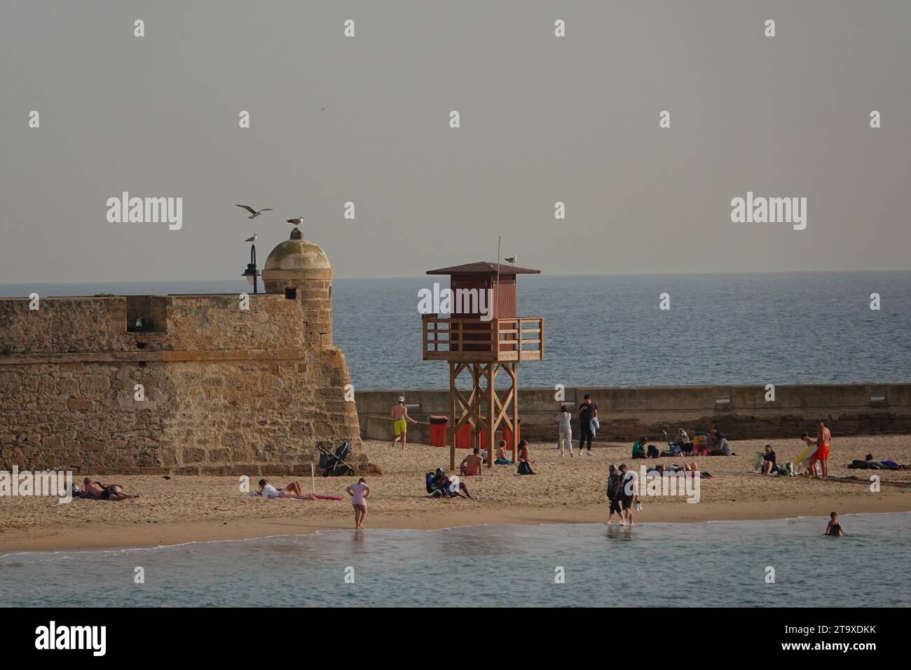 Gli amanti della spiaggia si rilassano vicino alle mura del Bastione di San Pedro a Cadice, in Spagna. La spiaggia pubblica si trova tra due antichi castelli sulla baia. Foto Stock