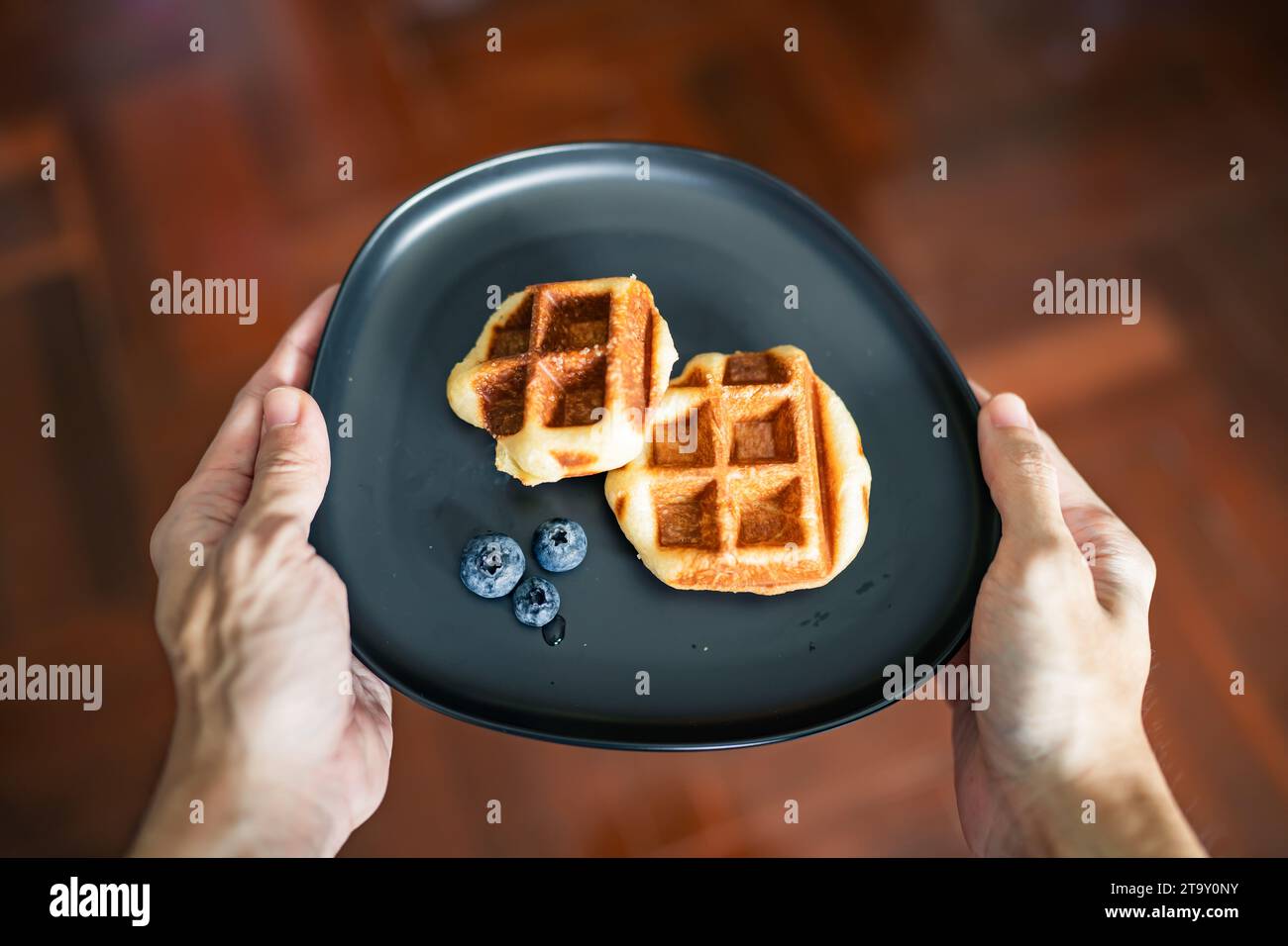 Waffle e mirtilli su un piatto in mano agli uomini Foto Stock