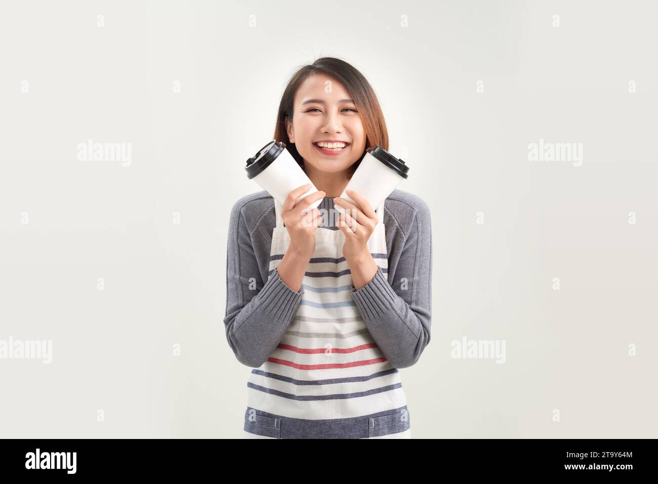 Simpatica e sorridente giovane donna asiatica in grembiule che regala caffè, tè e bevande calde Foto Stock