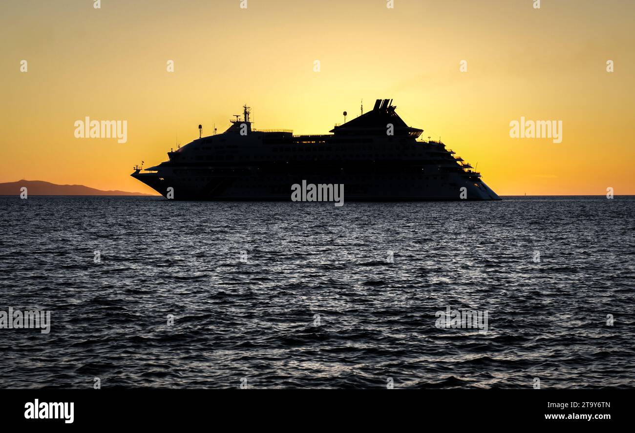 Sagoma scura della nave da crociera Celestial Crystal ancorata sull'isola di Mykonos durante un bellissimo tramonto arancione, le crociere della Grecia delle cicladi Foto Stock