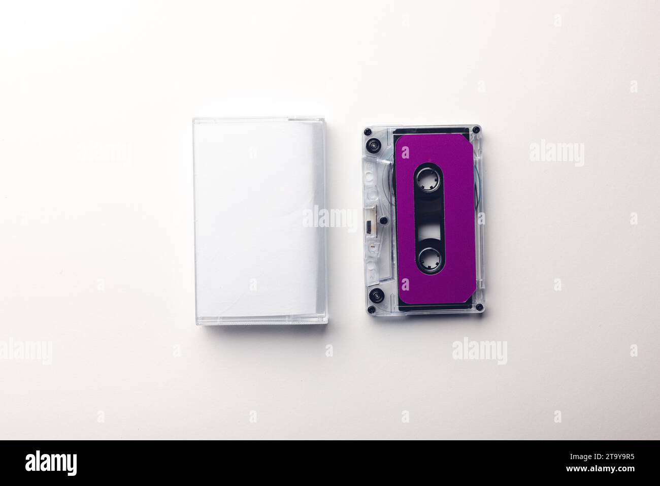 Vista dall'alto del nastro a cassetta viola e della scatola bianca disposti su sfondo bianco Foto Stock