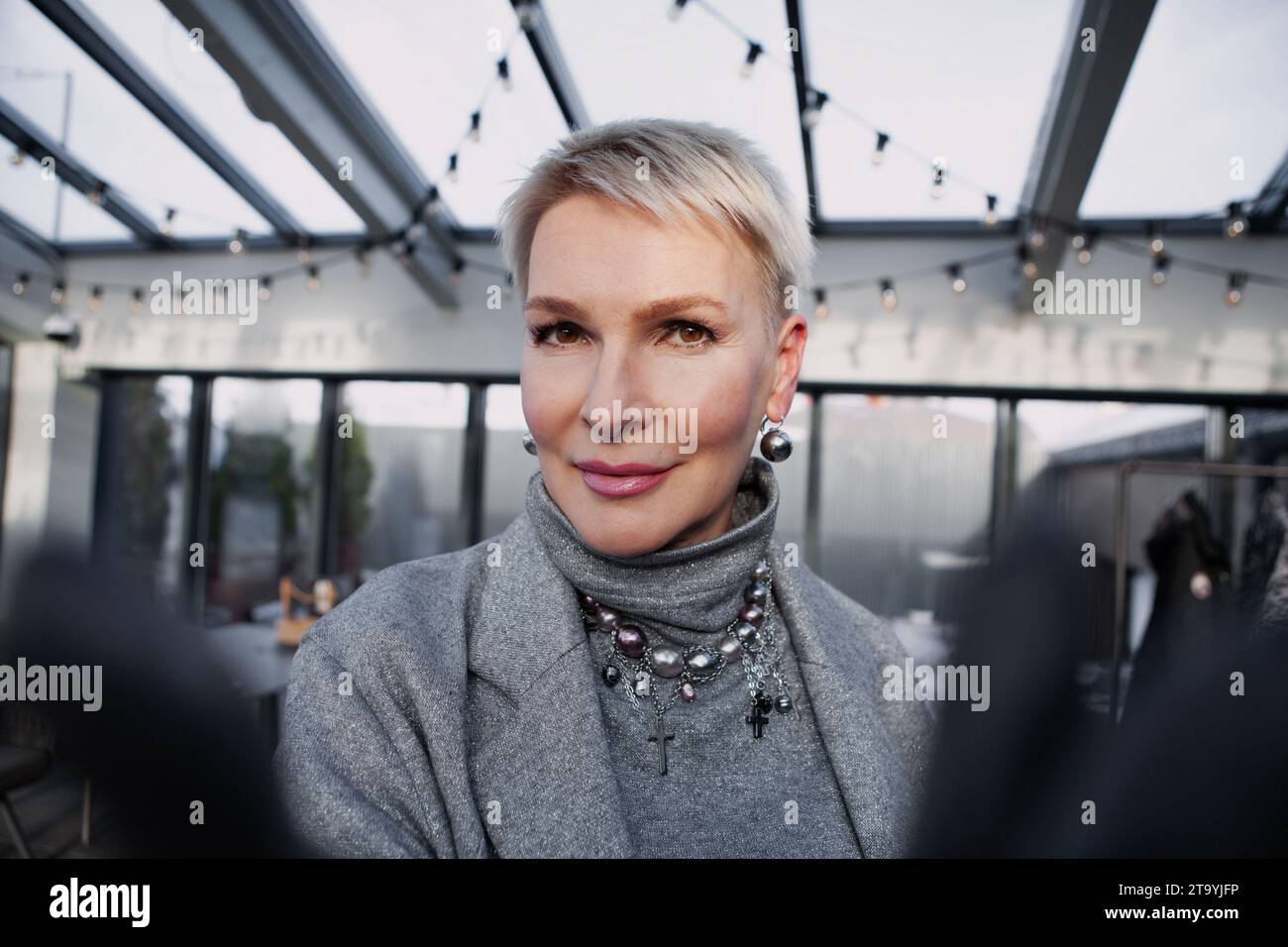 Selfie di bella donna bionda matura con taglio corto in abiti moderni e alla moda, dolcevita grigia, giacca. Ritratto ravvicinato elegante fe di mezza età Foto Stock