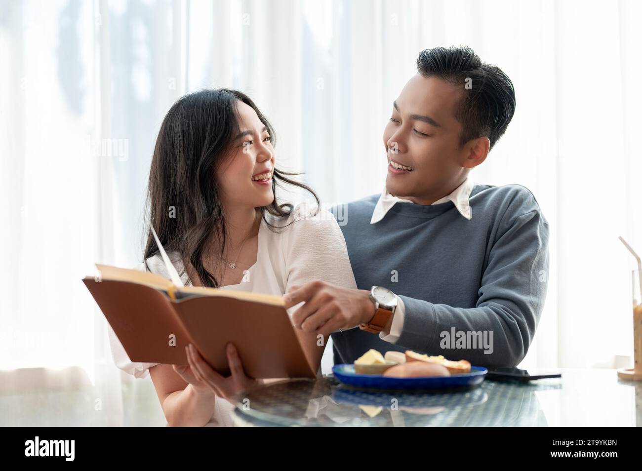 Giovane, bella e adorabile coppia asiatica che condivide il tempo libero insieme, leggendo libri in un grazioso caffè. Concetto di coppia. Foto Stock