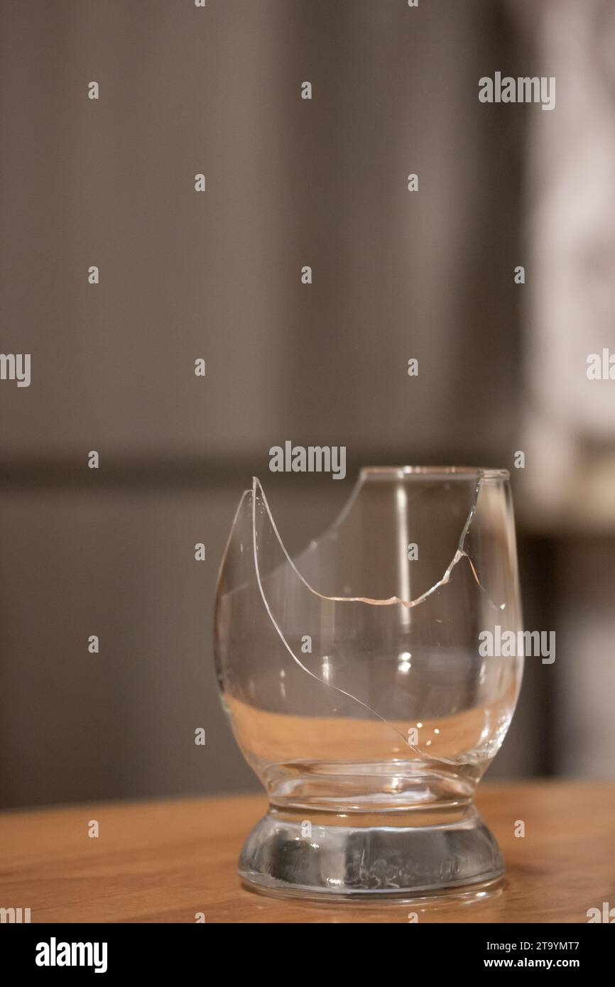 Bicchiere trasparente rotto sul tavolo. Pezzi taglienti e pericolosi in cucina. Immagine verticale Foto Stock