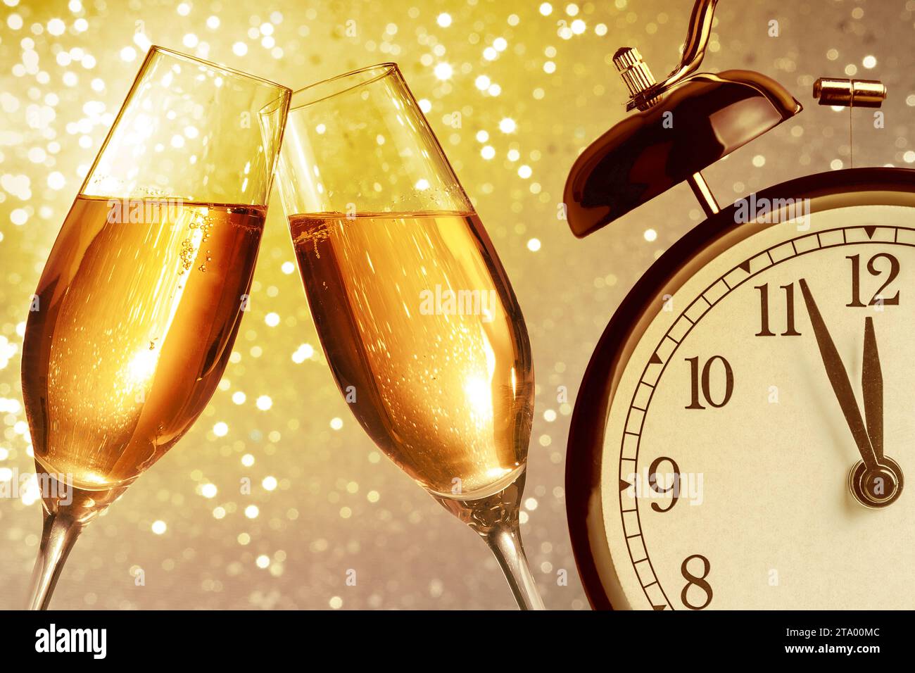 flauti di champagne con bollicine dorate fanno il tifo su sfondo bokeh chiaro dorato con sveglia vintage che mostra il concetto di happy new year a mezzogiorno o mezzanotte Foto Stock
