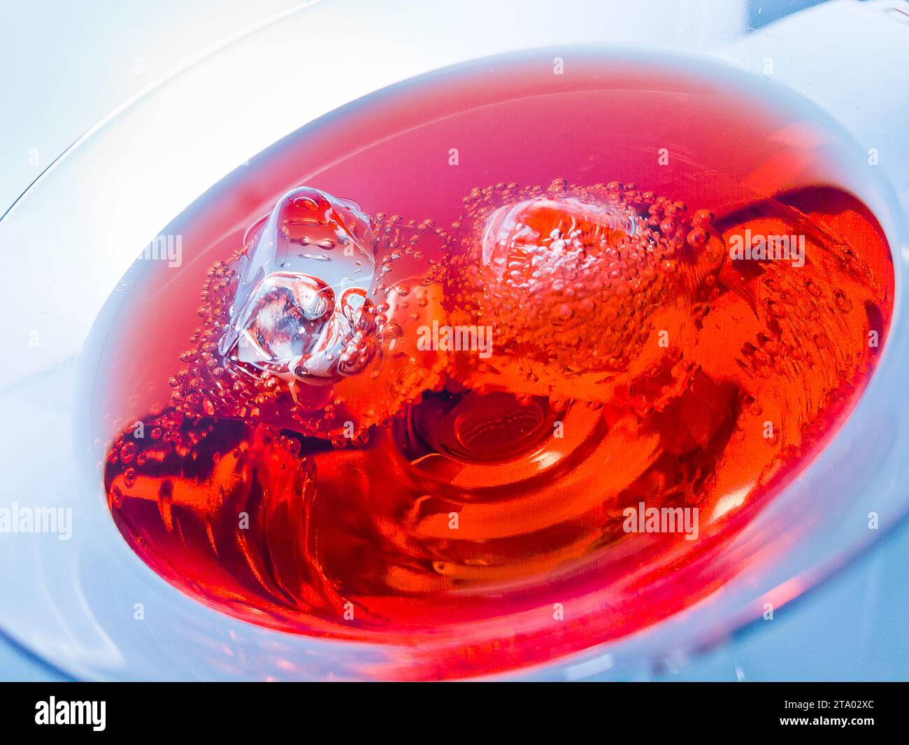 primo piano del cocktail rosso con cubetti di ghiaccio su sfondo blu chiaro, concetto di discoteca divertente e dance Foto Stock