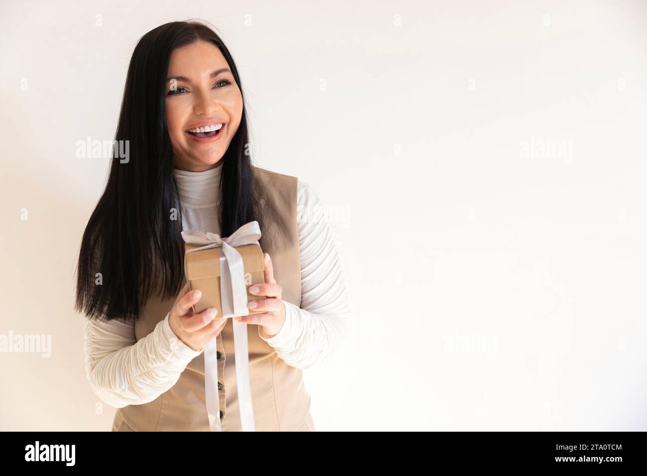 Ragazza attraente che tiene un regalo in mano e lo tiene alla fotocamera, concetto di festività e regali Foto Stock