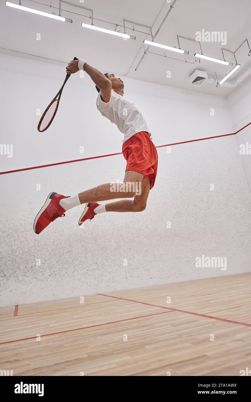 motion photo, sportivo afroamericano attivo che tiene racchetta mentre salta e gioca a squash Foto Stock
