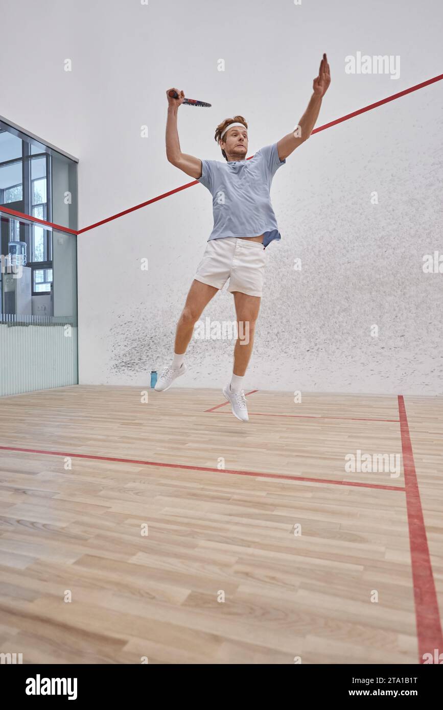 foto in movimento, divertente sportivo che tiene racchetta e salta mentre giochi a squash all'interno del campo Foto Stock