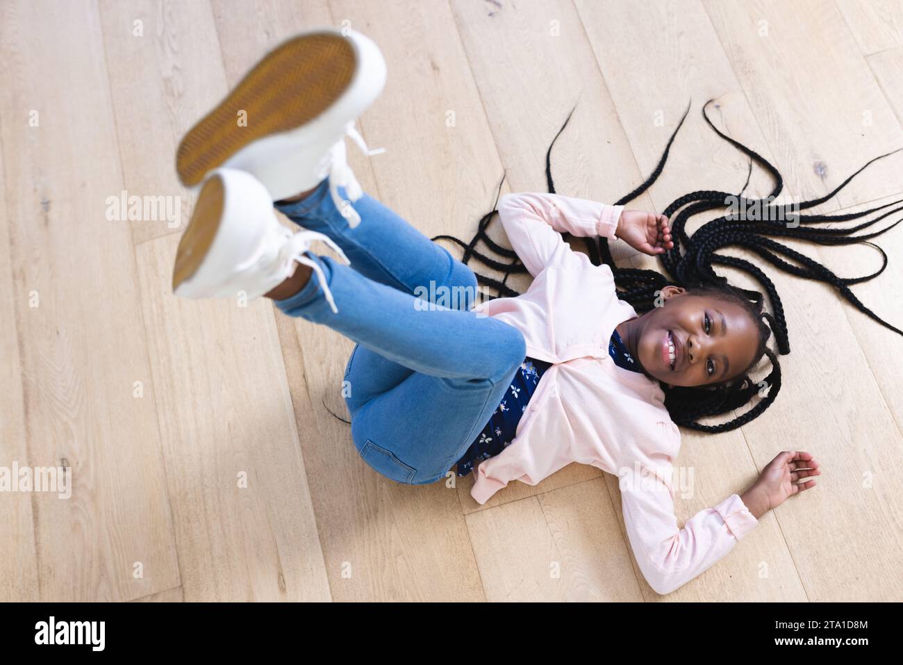 Felice ragazza afro-americana sdraiata sul pavimento con le gambe in aria a casa, spazio copia. Infanzia, espressione, gesticolazione e vita domestica, inalterati. Foto Stock