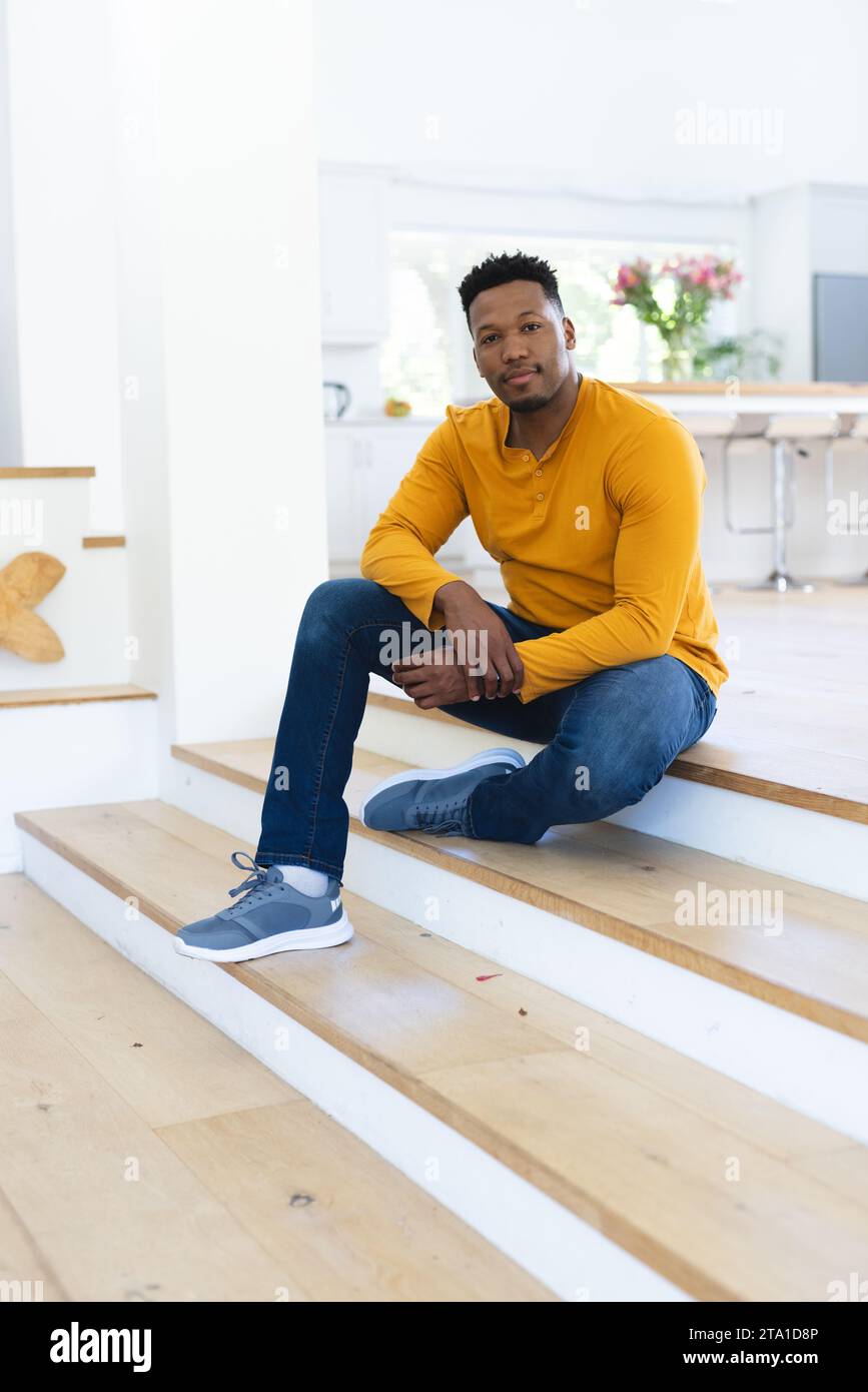 Uomo afro-americano seduto sulle scale a casa, spazio fotocopie. Espressione, gesticolazione e vita domestica, inalterata. Foto Stock