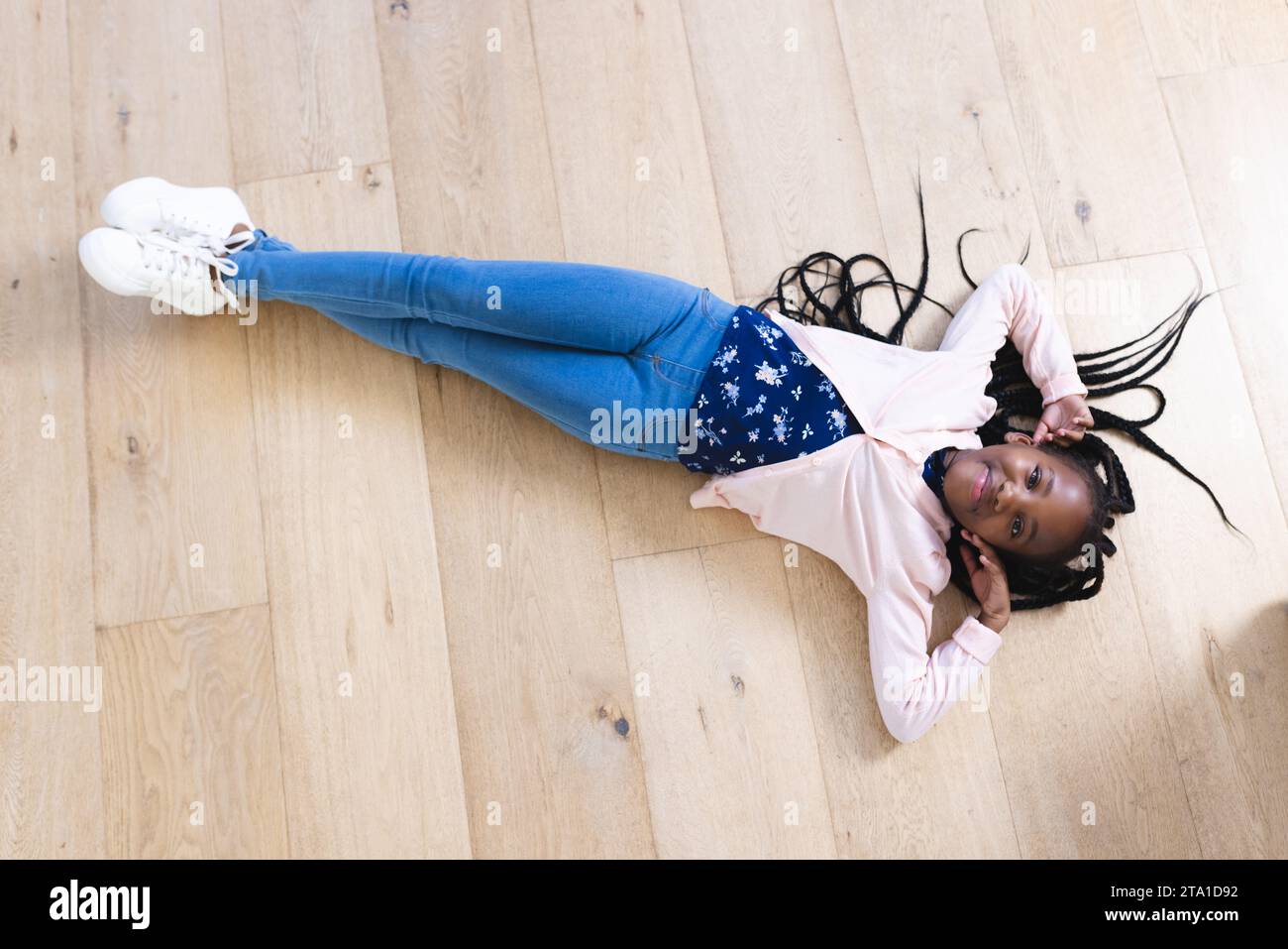 Felice ragazza afro-americana sdraiata sul pavimento con le mani sul viso a casa, spazio copia. Infanzia, espressione, gesticolazione e vita domestica, inalterati. Foto Stock