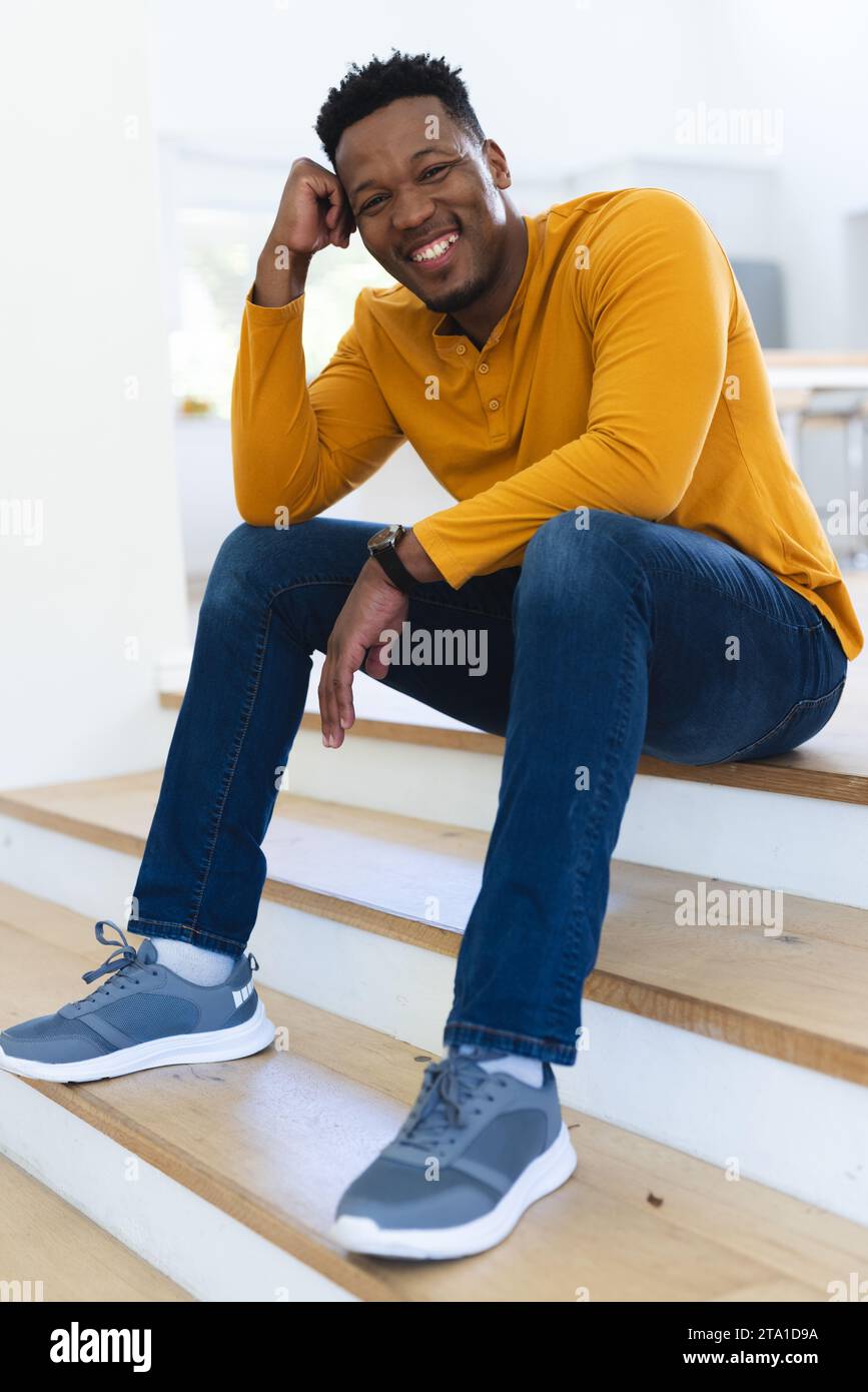 Felice afro-americano seduto sulle scale con il pugno in faccia a casa, spazio per le copie. Espressione, gesticolazione e vita domestica, inalterata. Foto Stock