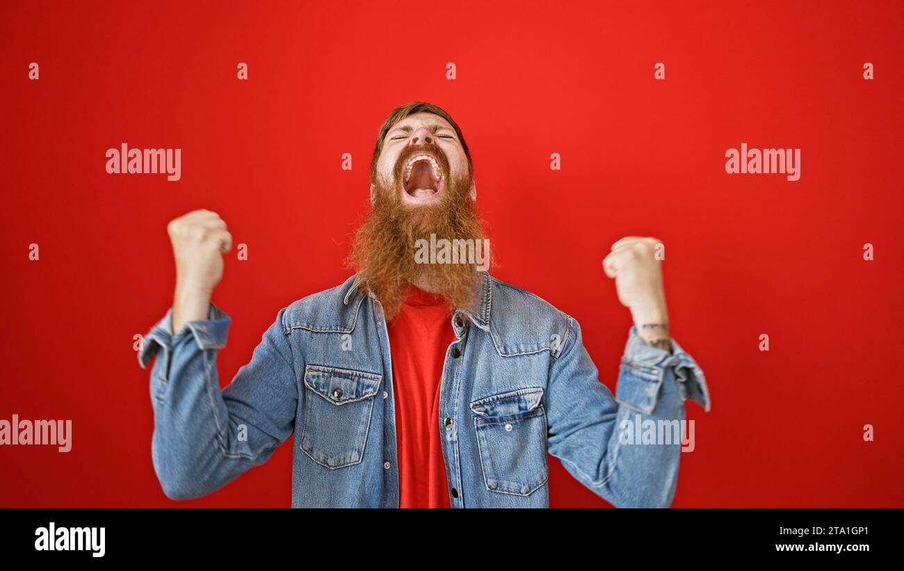 Giovane uomo rosso sicuro di sé, traboccante di gioia e positività, in piedi in modo casual, festeggia felicemente su uno sfondo rosso isolato, il suo wi-fi Foto Stock