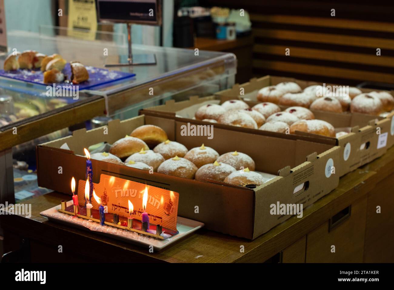 Una menorah Hanukkah brucia in una panetteria di Gerusalemme che vende ciambelle ricoperte di zucchero durante la celebrazione dell'Hanukkah, il Festival delle luci in Israele. Foto Stock