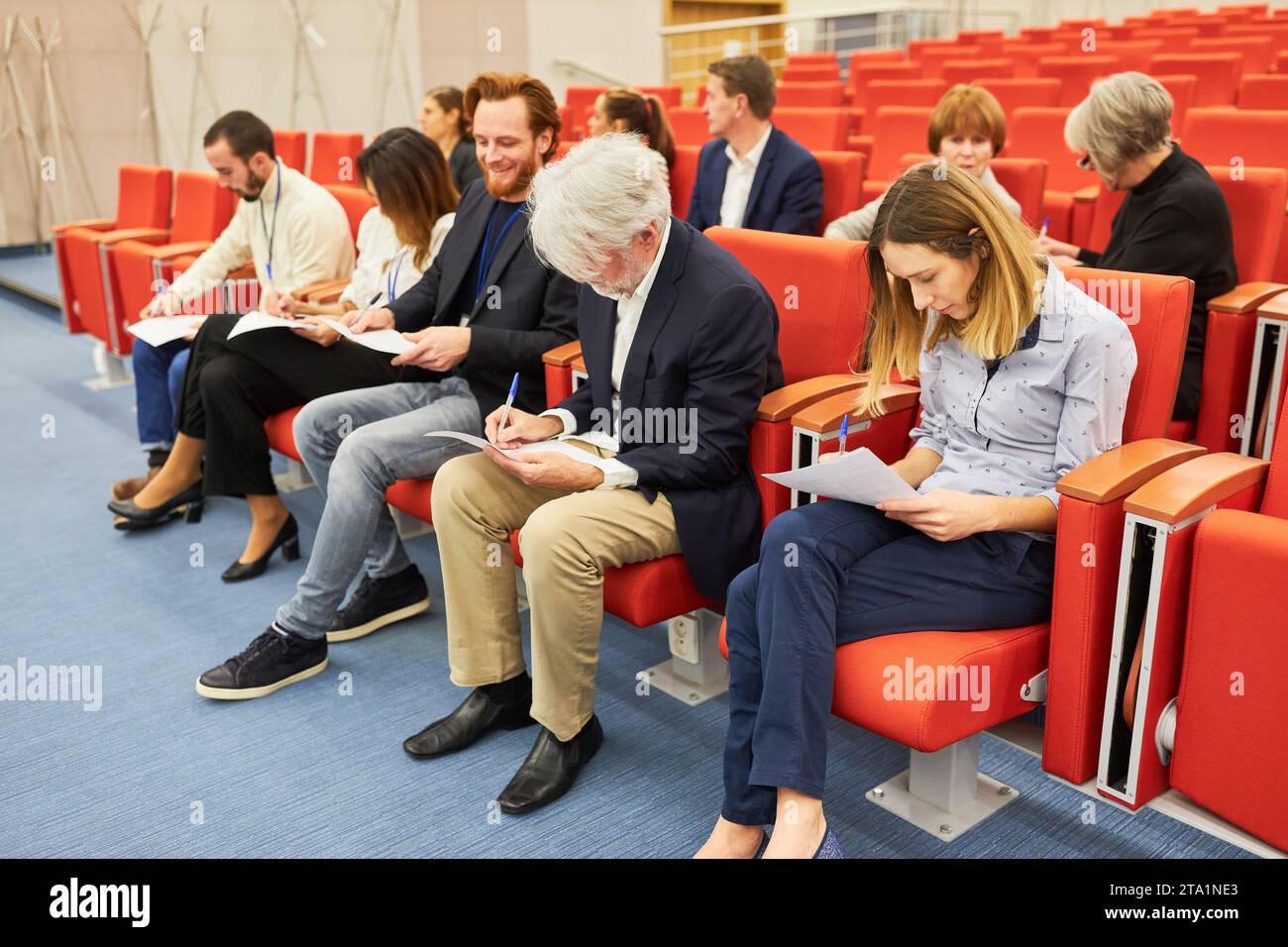 Un pubblico maschile e femminile che scrive documenti mentre è seduto al centro congressi Foto Stock