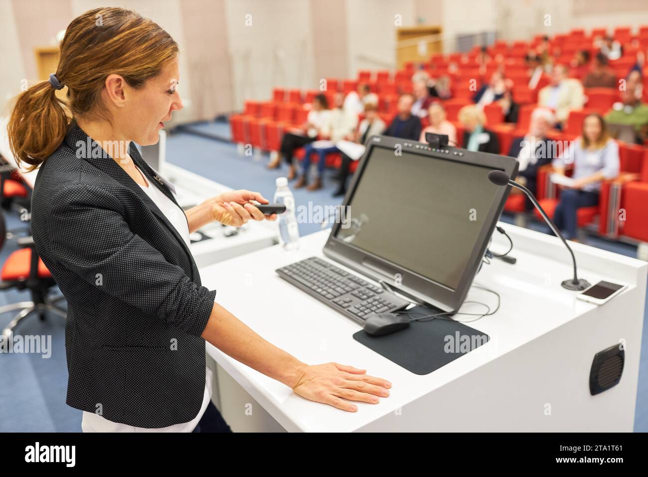 Oratrice donna che tiene una presentazione sul palco durante una sessione d'affari nel centro congressi Foto Stock