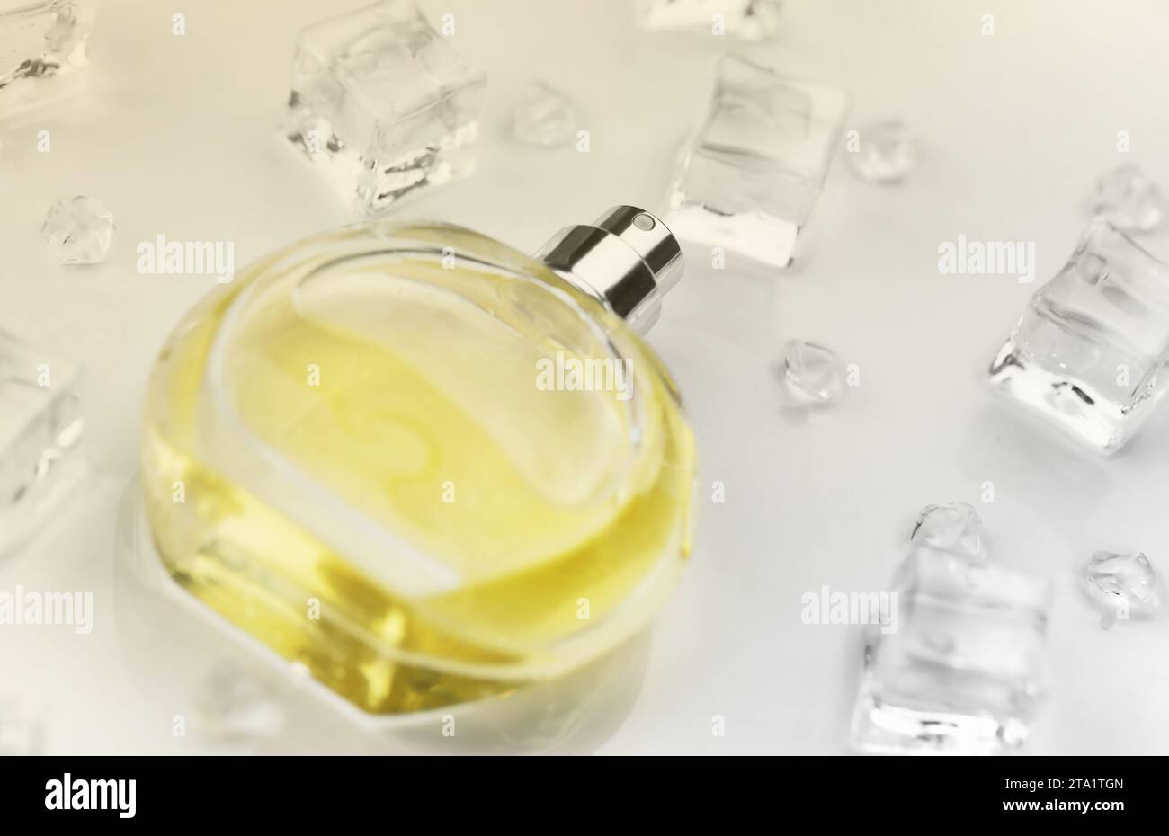 Bottiglia gialla di profumo femminile, fotografia oggettiva della bottiglia di profumo in cubetti di ghiaccio e acqua su tavolo bianco. Vista dall'alto. Foto del prodotto mockup, concetto di freschezza e aroma Foto Stock