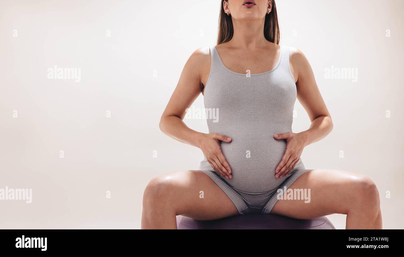 donna incinta nel suo terzo trimestre pratica yoga prenatale in uno studio. Utilizzando una palla di stabilità come supporto, si concentra sulla flessibilità e sulla forza Foto Stock
