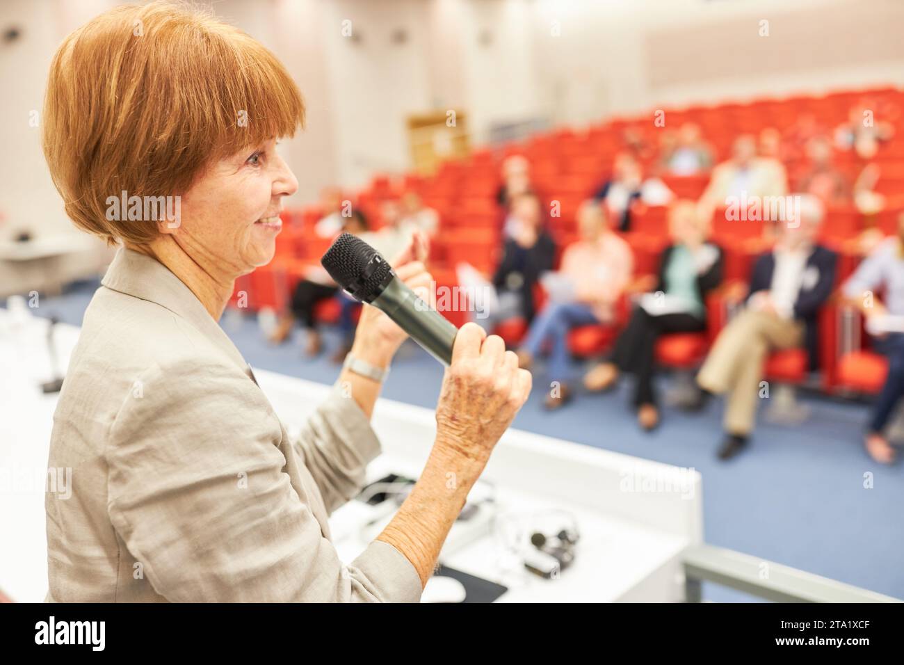 Oratrice femminile sul palco che parla a un evento pubblico con persone nel centro congressi Foto Stock