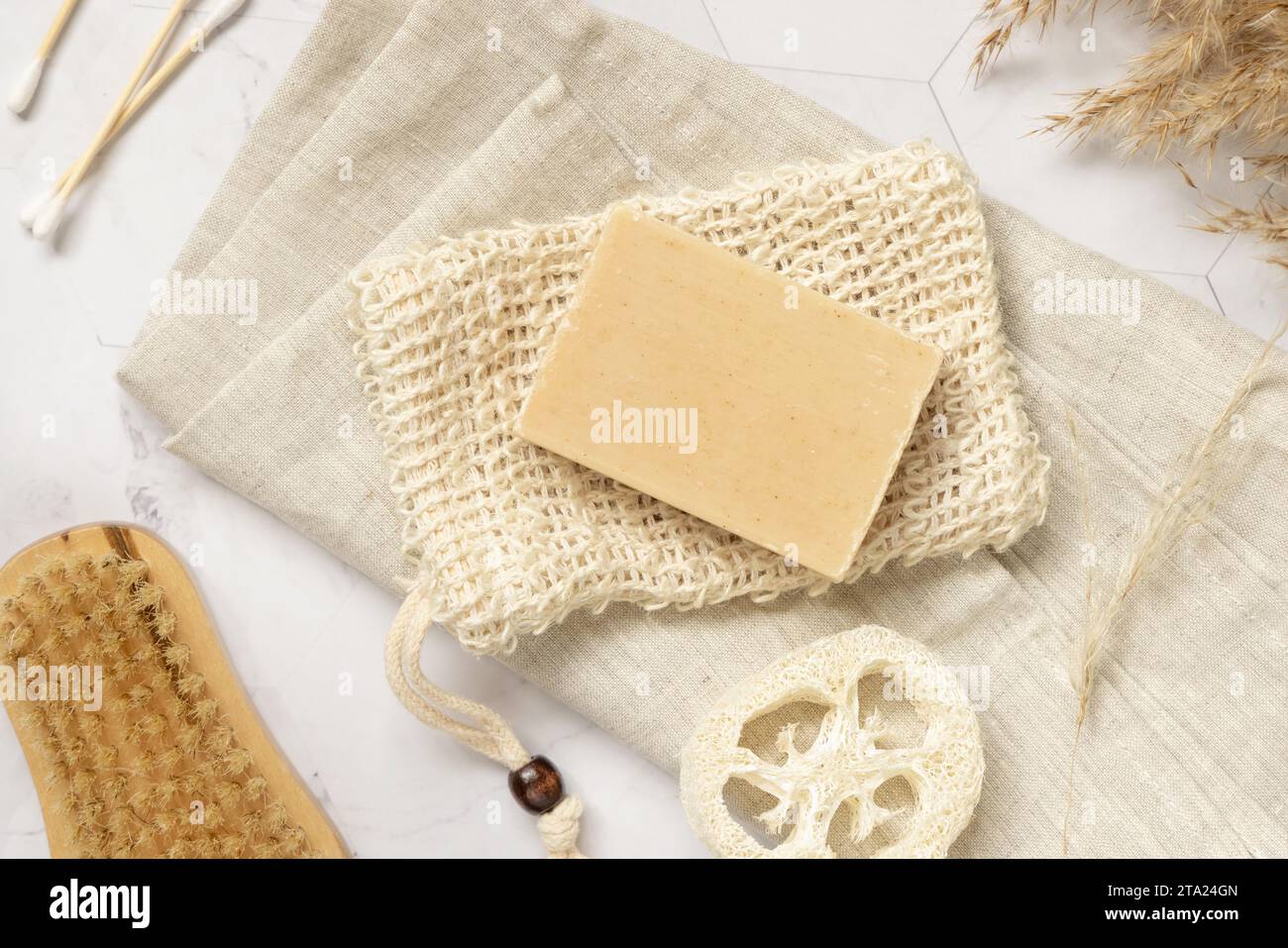 Sapone beige su un sacchetto salvasapone vicino alla spugna naturale e pennello su marmo bianco, vista dall'alto, spazio per copia. Prodotto a base di erbe naturale per la cura del viso e del corpo Foto Stock