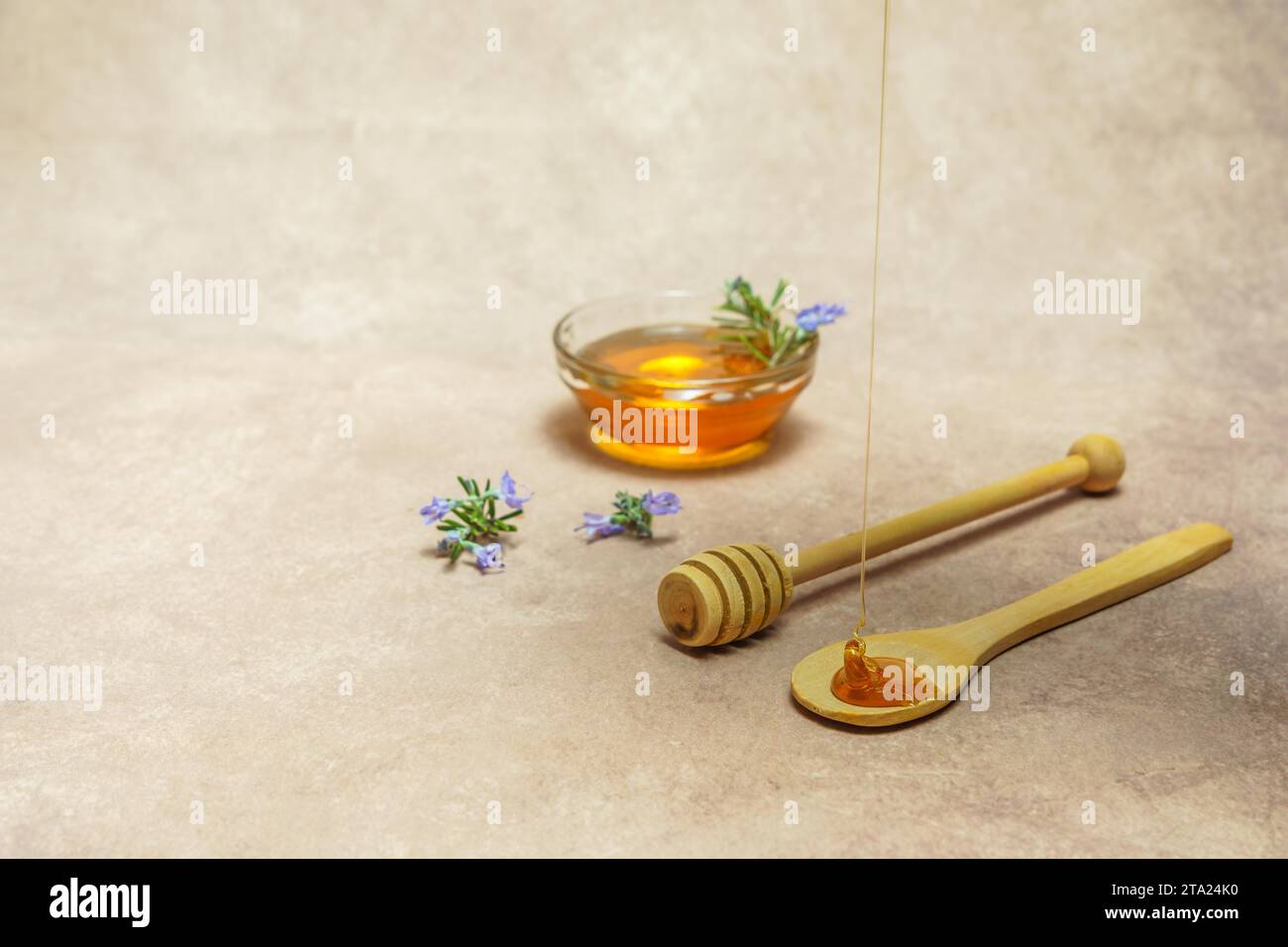 Miele di rosmarino naturale che gocciola su un cucchiaio di legno con rami di fiori di rosmarino e una ciotola con miele Foto Stock
