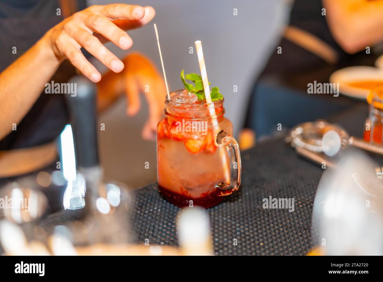 Primo piano di un cocktail di margarita rosso mezcal guarnito con menta nel bancone di un bar mentre il barista lo prepara Foto Stock